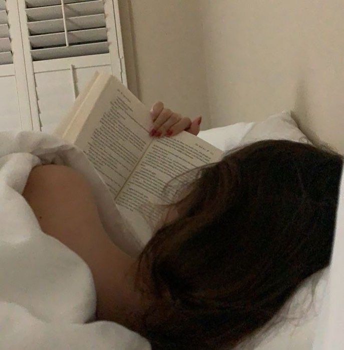 a woman laying in bed with her head on the pillow and holding an open book