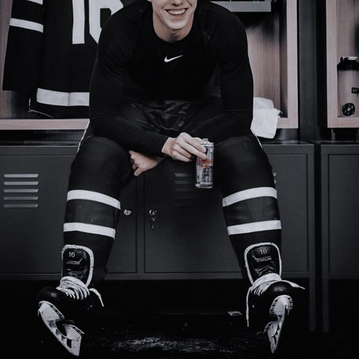 a man sitting on top of lockers with hockey socks and holding a drink in his hand