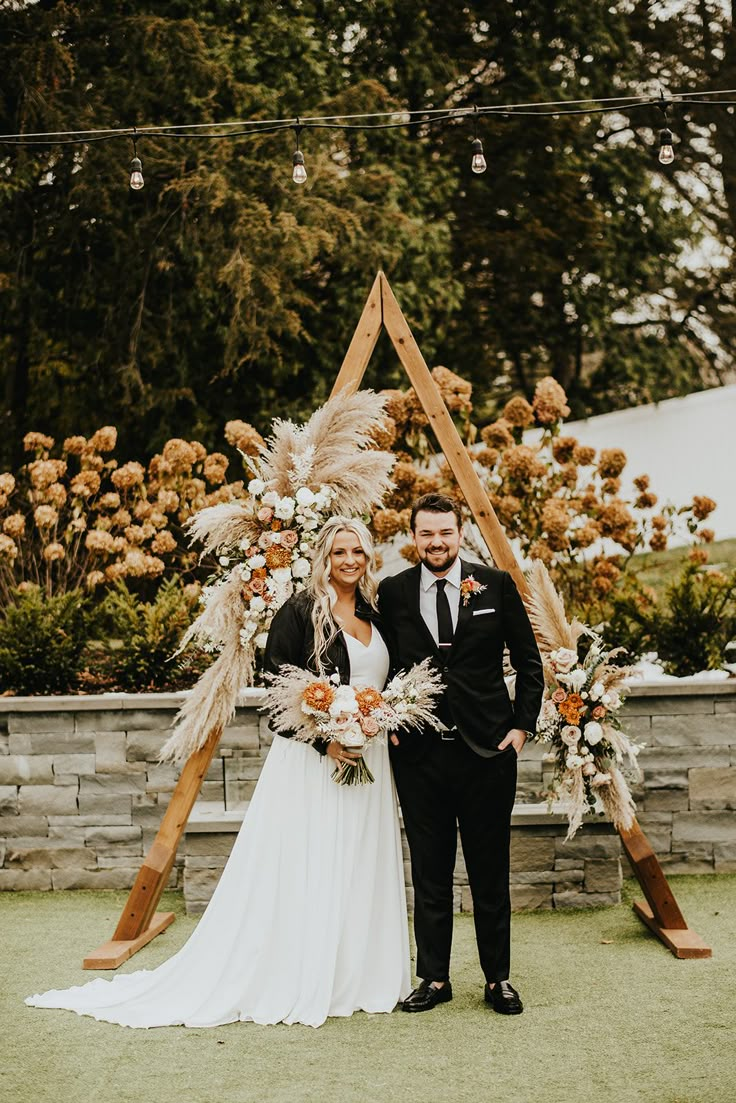 a man and woman standing next to each other in front of a wooden arch decorated with flowers