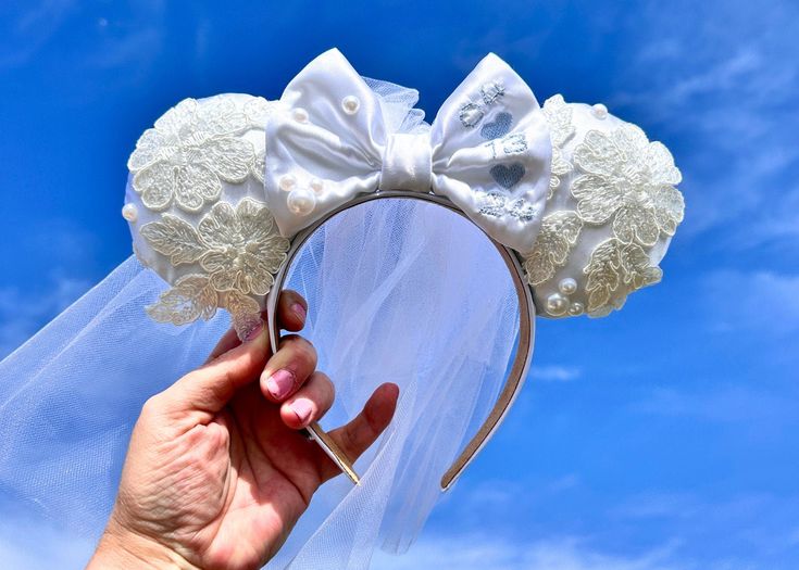 a hand is holding up a white headband with flowers on it and a veil in the background