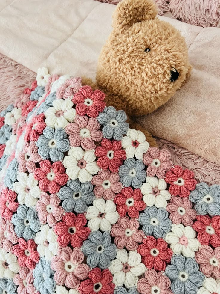 a teddy bear laying on top of a bed covered in crocheted blankets and pillows