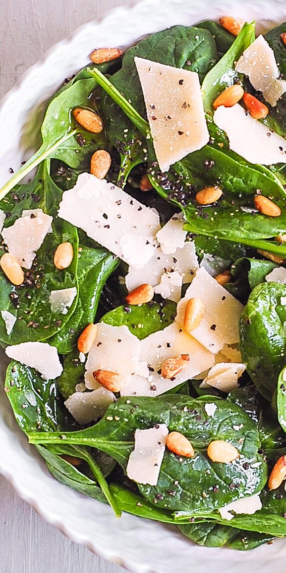 spinach salad with cheese and pine nuts in a white bowl