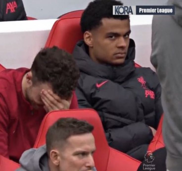 two men sitting next to each other at a soccer game, one is covering his face