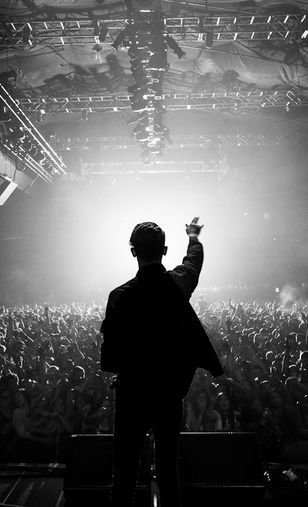 a man standing in front of a crowd at a concert with his hand up to the sky