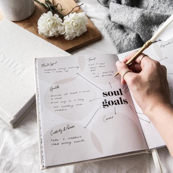 a person is writing on a book with flowers in the background and a pen next to it