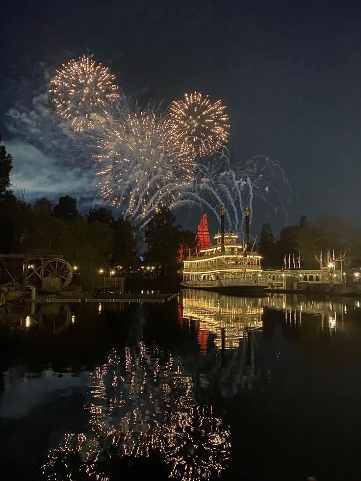 fireworks are lit up in the night sky above a river with boats and ferris wheel