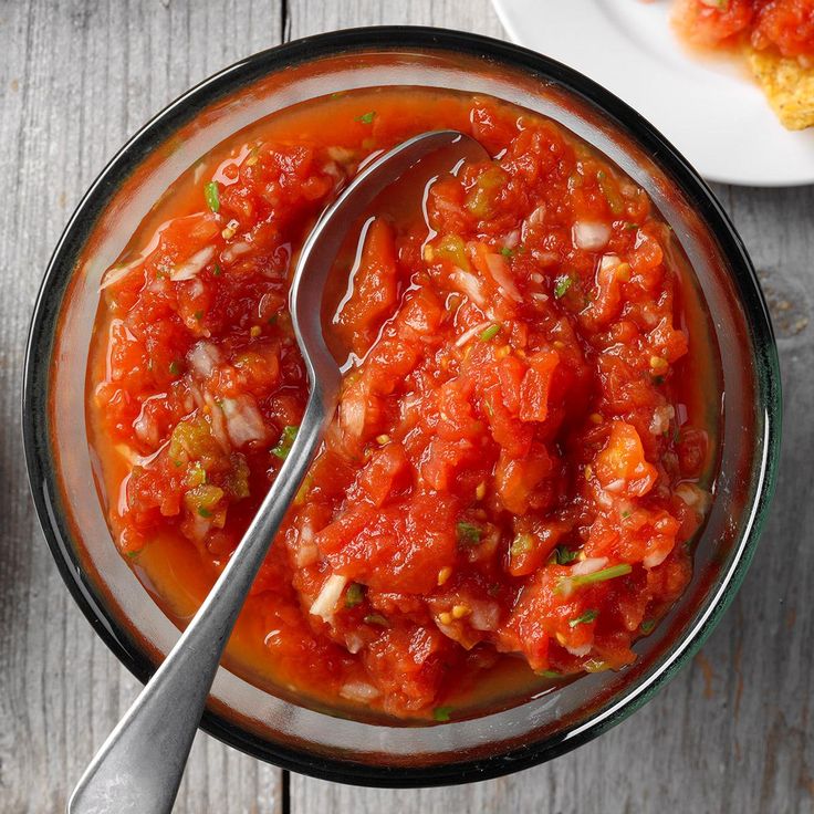 a bowl filled with tomato sauce next to two plates of food on a wooden table