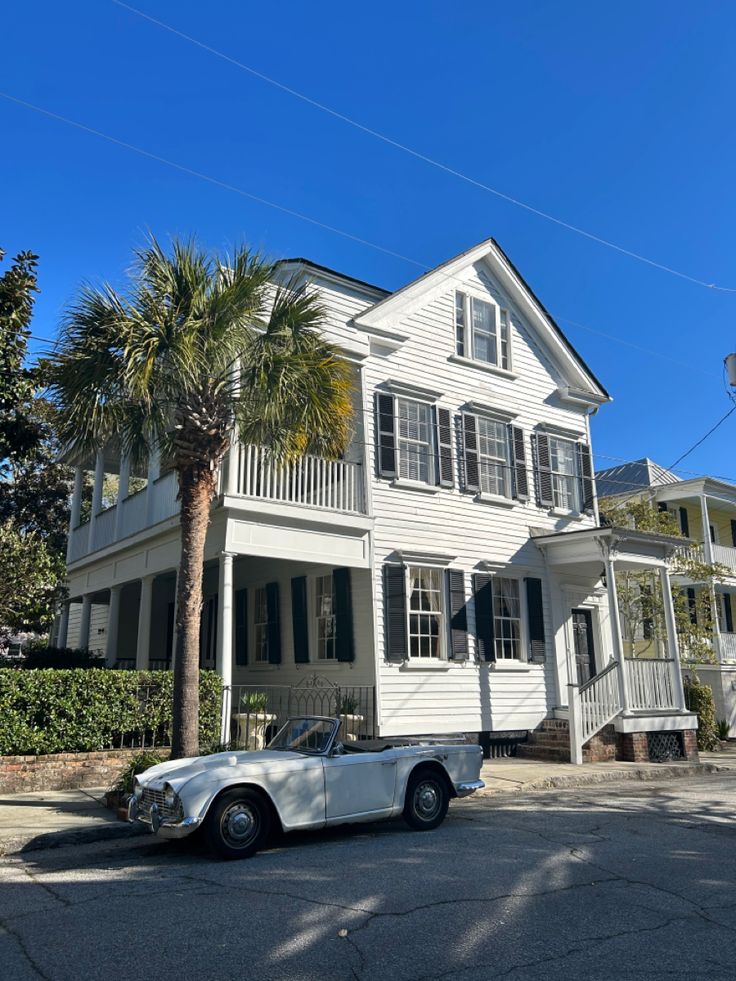 an old car parked in front of a white house with palm trees on the street