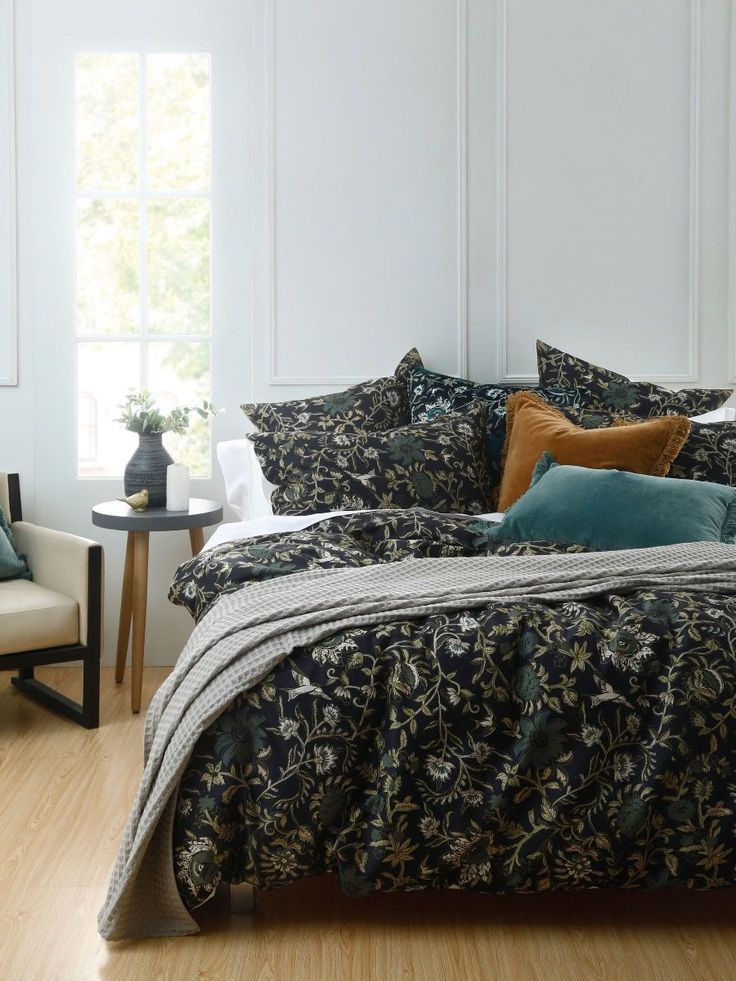 a bedroom with white walls and wood flooring has a black floral comforter on the bed