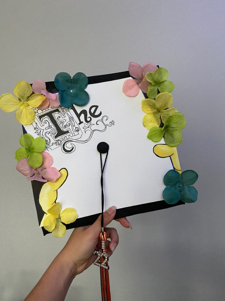 a hand holding a graduation cap with flowers on it