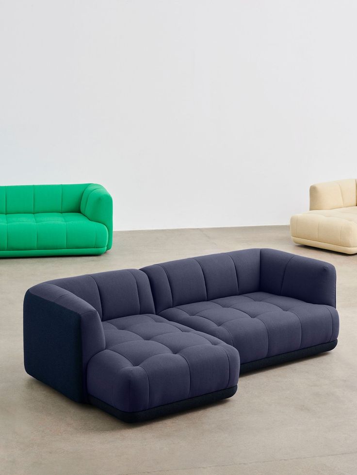 three different colored couches in an empty room with white walls and concrete flooring