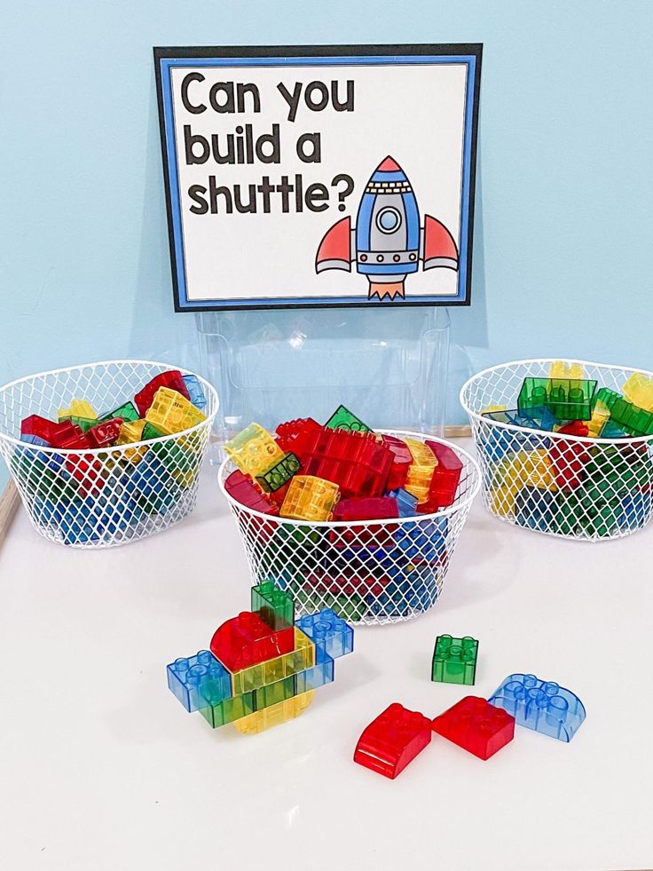 three baskets filled with legos sitting on top of a table next to a sign that says can you build a shuttle?