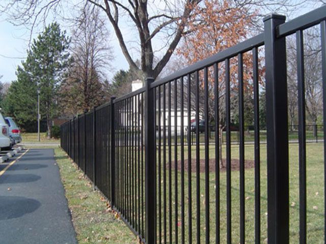 a black metal fence next to a street with cars parked on the side of it