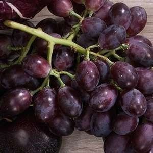 a bunch of purple grapes sitting on top of a wooden table next to an eggplant