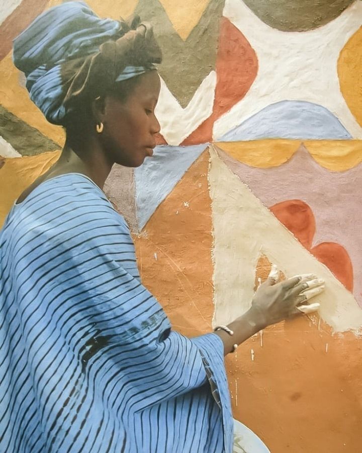 a woman sitting on top of a white chair in front of a colorful wall