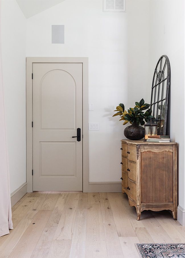 a white room with a wooden dresser and mirror on the wall next to a door