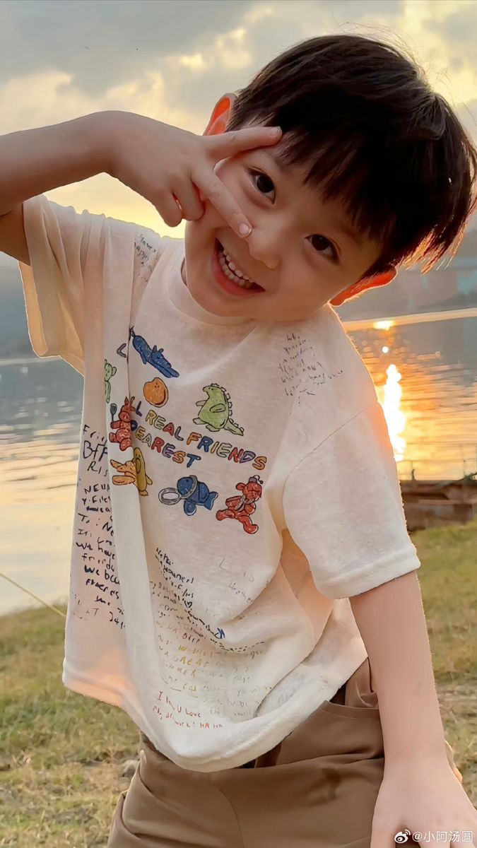 a young boy standing next to a body of water with his hand on his head