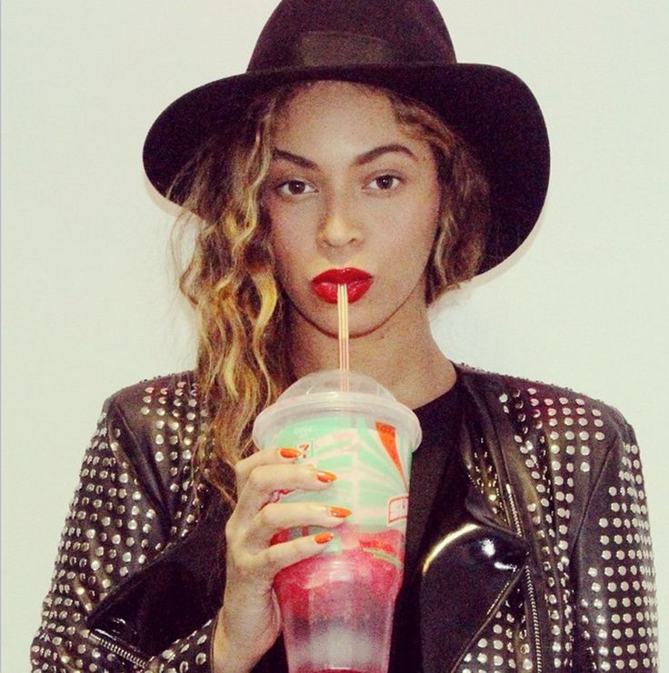 a woman in a black hat drinking from a plastic cup with a straw and holding a drink