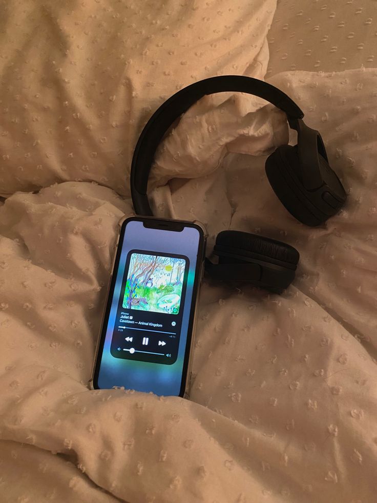 a cell phone laying on top of a bed next to headphones