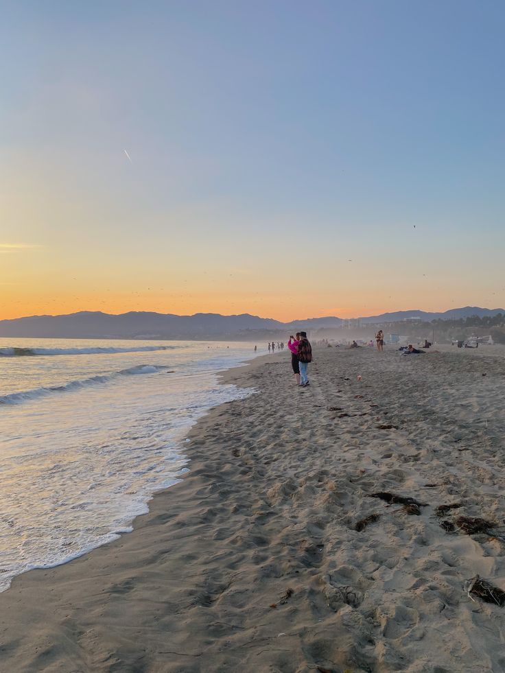 two people walking on the beach at sunset