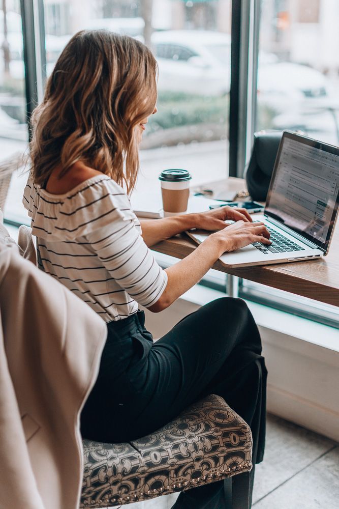 a woman sitting at a table with a laptop computer on her lap and looking out the window