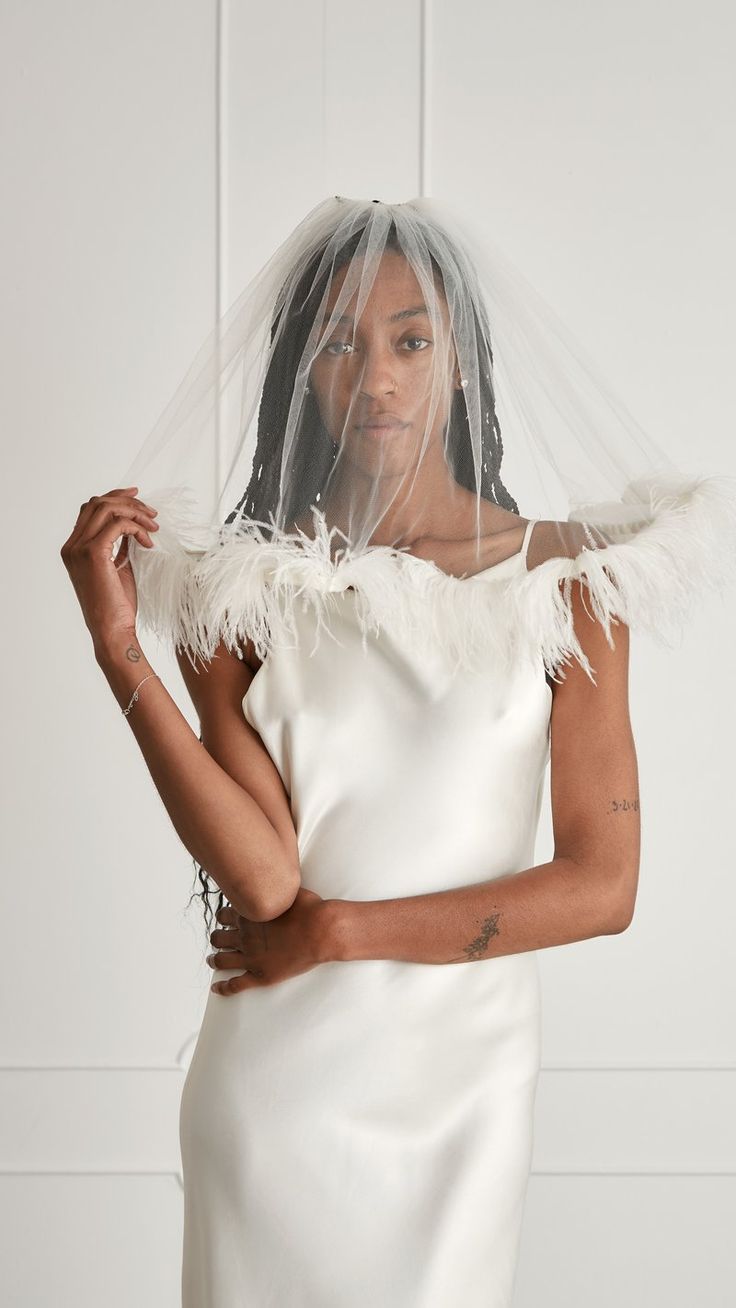 a woman in a white dress with a veil on her head and hands behind her back