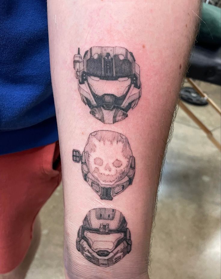 three different tattoos on the arm of a person's left leg, including a skull and helmet