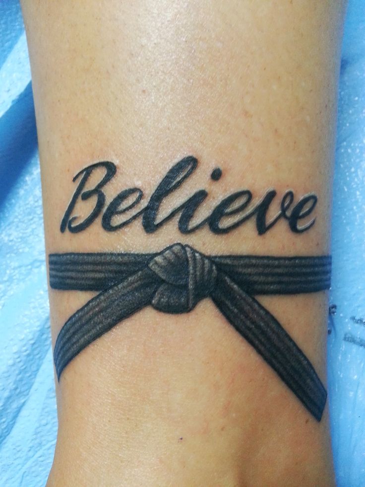 a wrist tattoo with the words believe and a ribbon tied around it on someone's foot