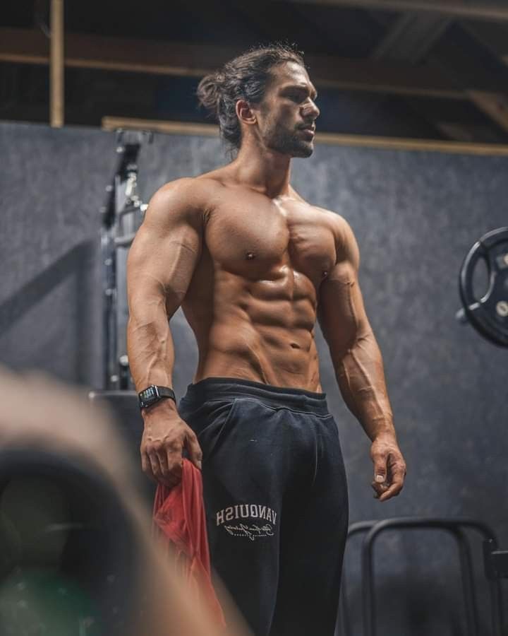 a man with no shirt standing in front of a gym equipment rack and looking off to the side