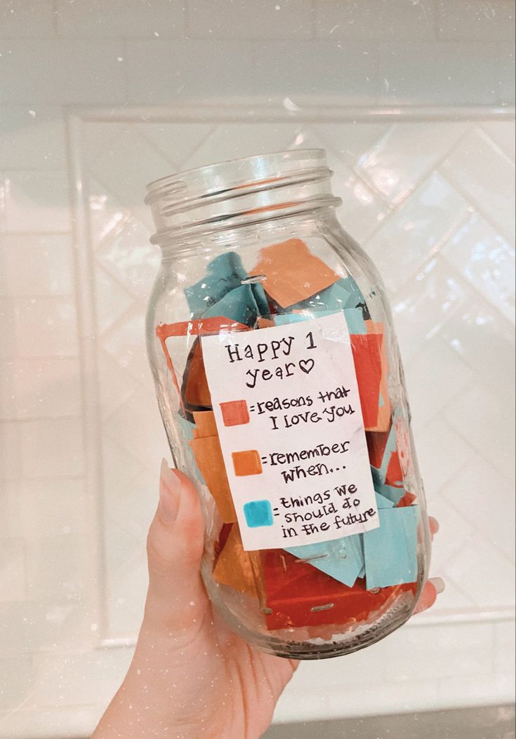 a person holding a jar filled with colorful pieces of paper and some words on it