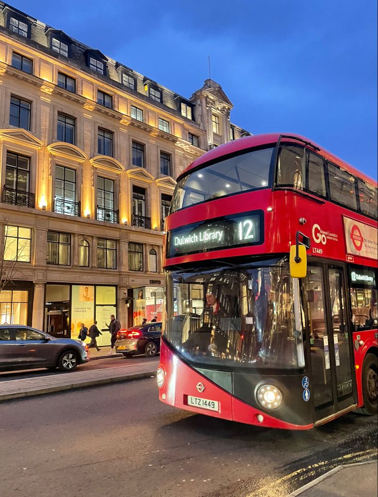 a red double decker bus driving down a street in front of tall buildings at night