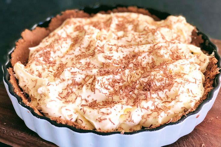 there is a pie with white frosting in the pan on top of a wooden table