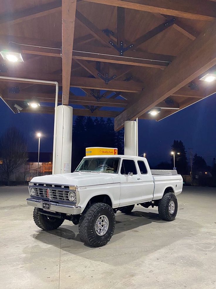 a white pick up truck parked under a covered structure at night with its lights on