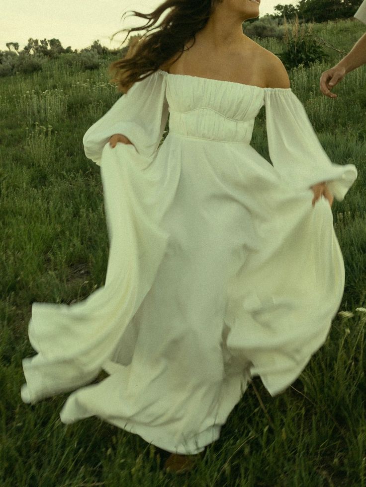 a woman in a white dress is walking through the grass