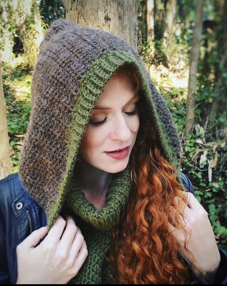 a woman with red hair wearing a green knitted hood and scarf in the woods