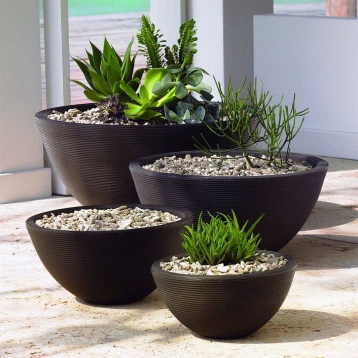 four planters with plants in them sitting on the ground next to a door way