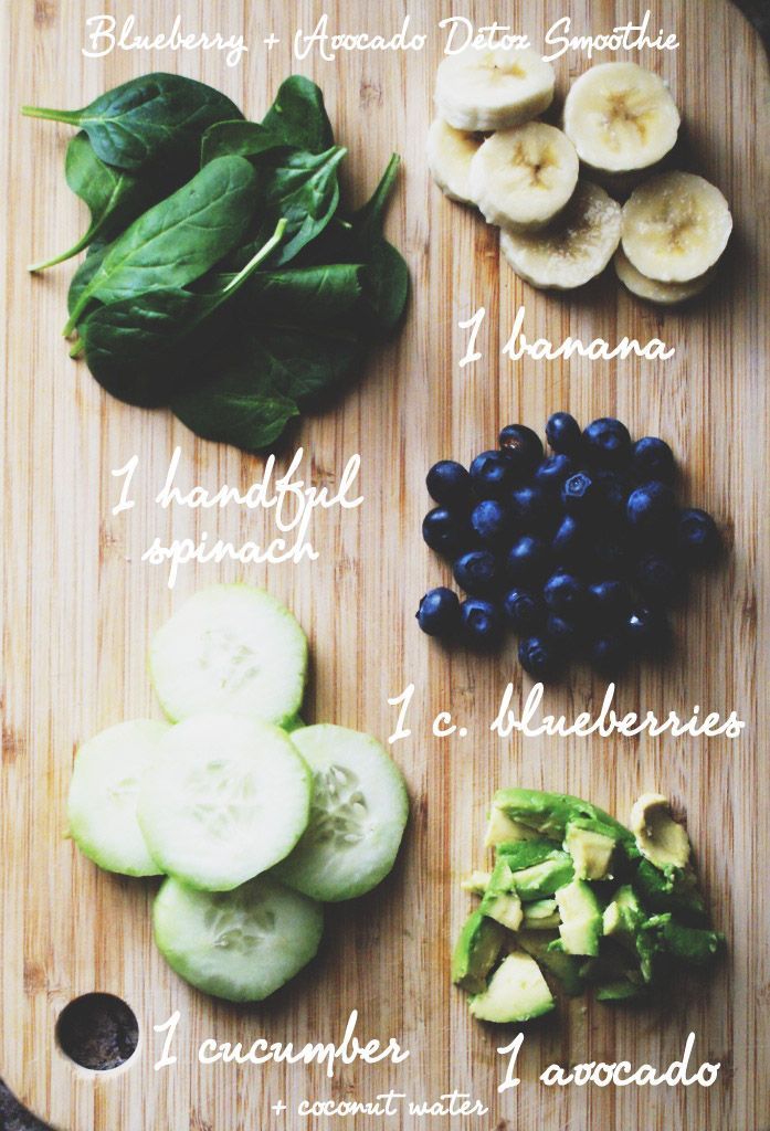 a cutting board topped with cucumbers, blueberries, and spinach on top of a wooden table