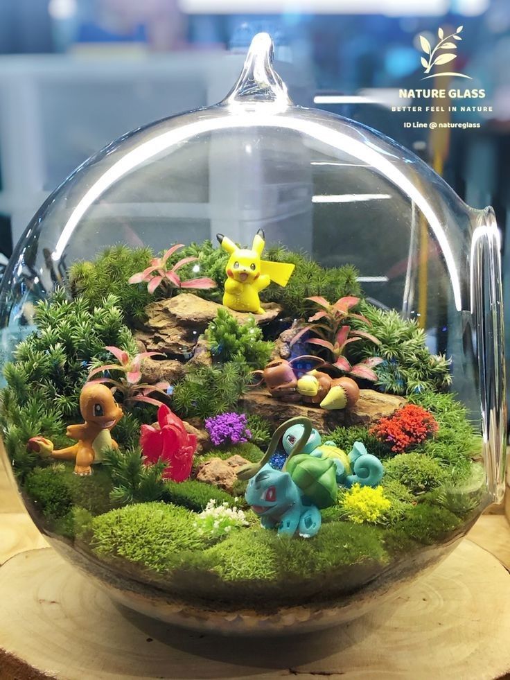 a glass bowl filled with small figurines on top of a wooden base covered in moss