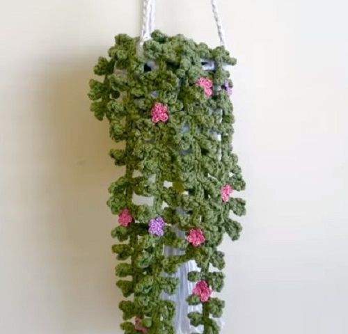 a crocheted bag hanging from a hook on a wall with pink and green flowers