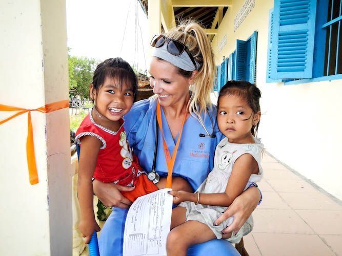 a woman in scrubs sitting on a bench with two children and an orange ribbon around her neck