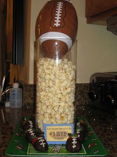 a football in a jar filled with popcorn and chocolate candies on a green tray