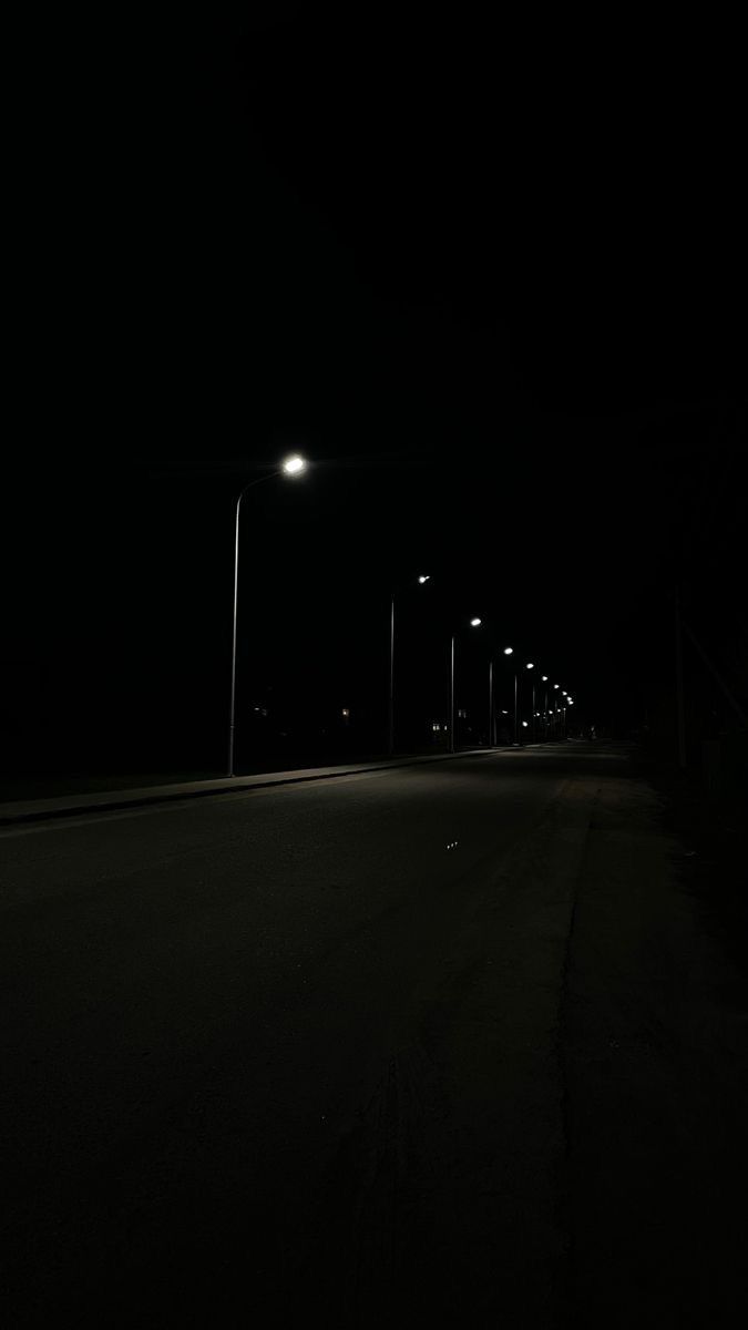 an empty road at night with street lights in the dark and no cars on it