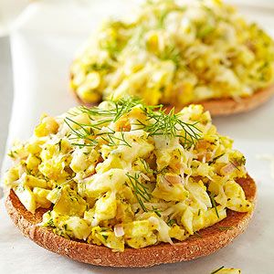 two open faced sandwiches with scrambled eggs and dill sprig on top, sitting on a white napkin