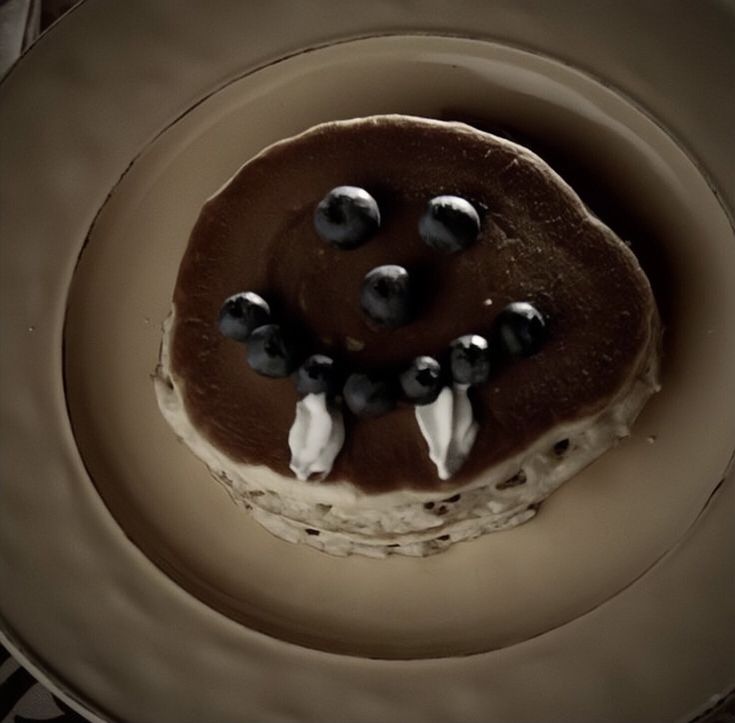 a cake with chocolate icing and blueberries on top is sitting on a plate