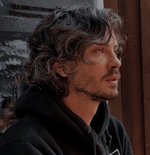 a man with long hair wearing a black hoodie and looking off into the distance