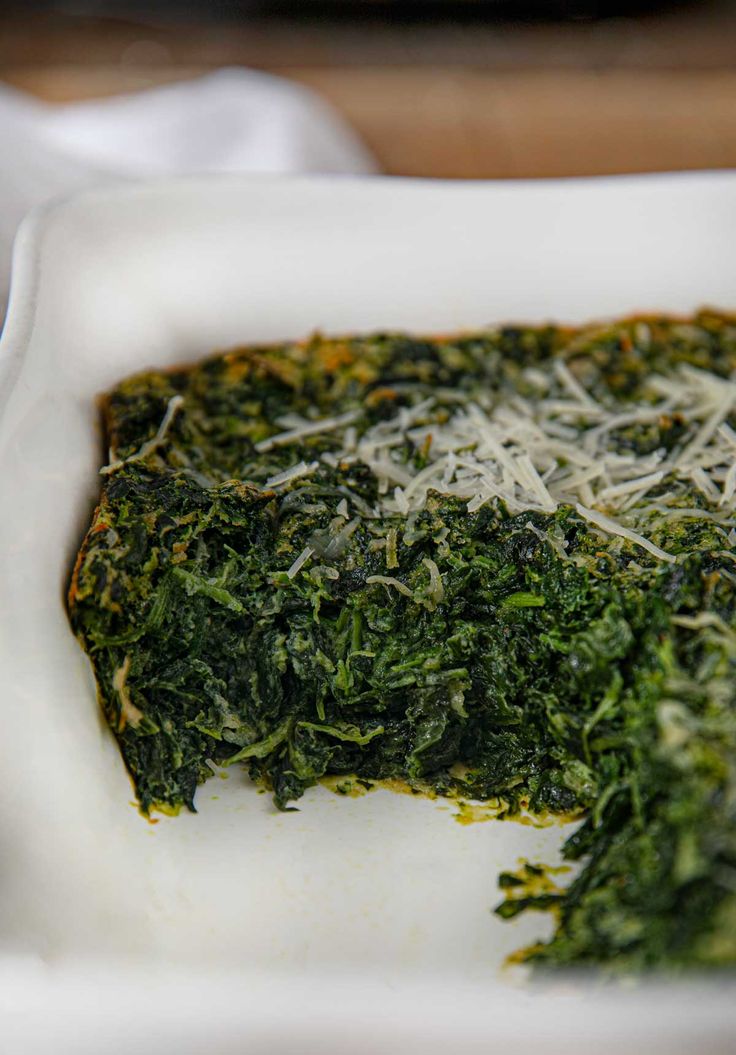 a white dish filled with spinach and parmesan cheese on top of it