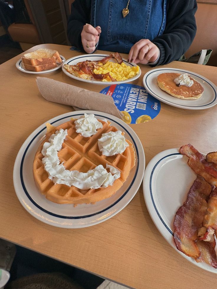 a person sitting at a table with plates of breakfast food on it and bacon in front of them