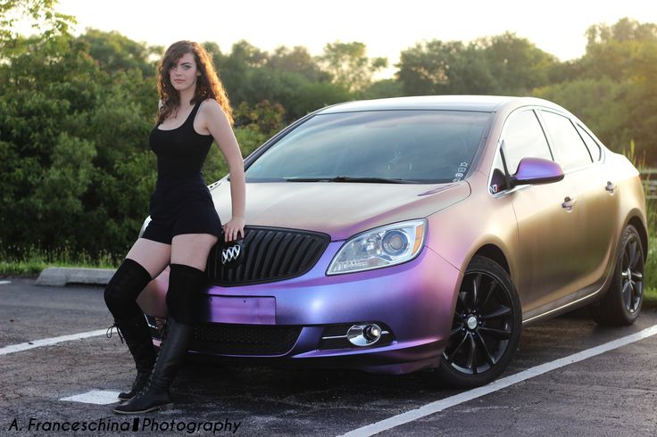 a woman standing next to a car in a parking lot with her leg on the hood