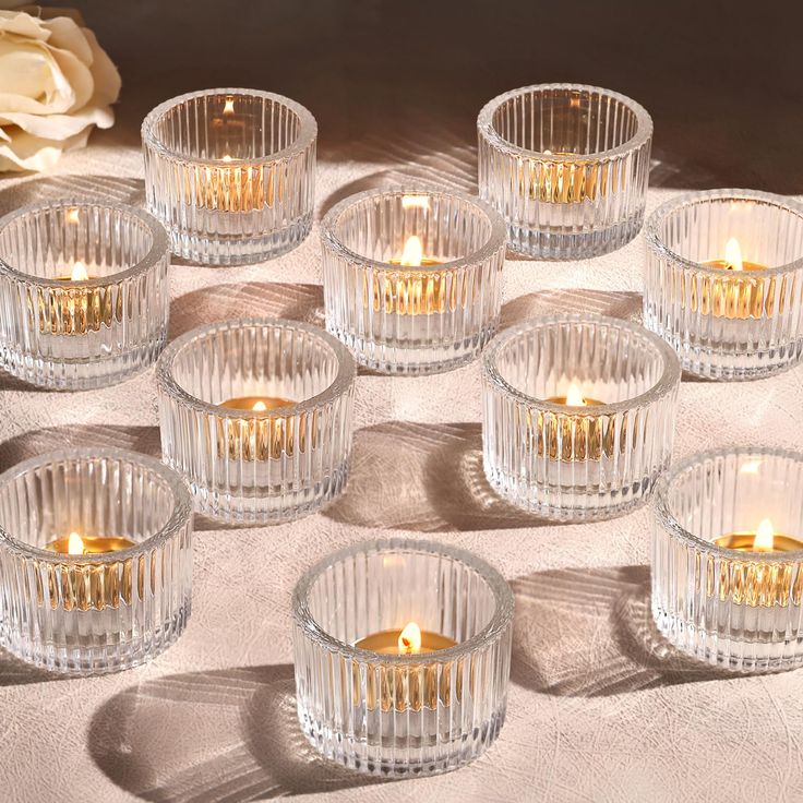 many clear glass bowls with lit candles in them on a white table cloth next to a rose