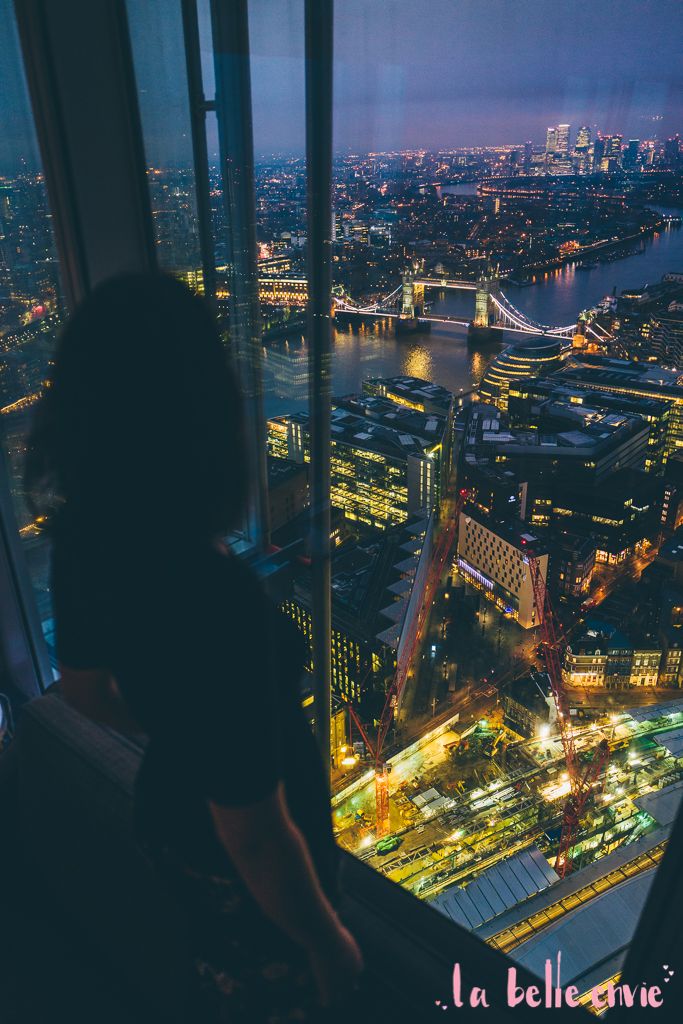 a woman looking out over the city at night from an observation tower in london, england